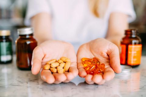 Two hands, one holding vitamins, the other holding gel vitamins, with pill bottles nearby