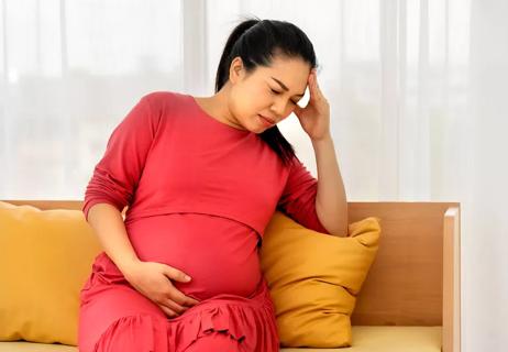 Pregnant woman with headache sitting on couch