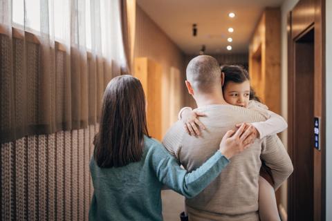 Caregiver carrying child, with other caregiver walking with arms around them, walking down hotel hallway