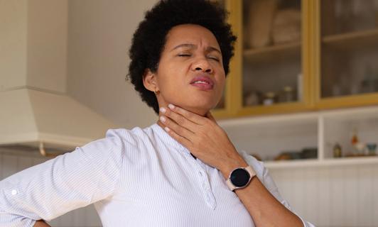 Person holding hand up to their throat, grimacing