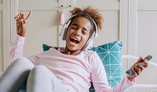 Child on bed and pillow, with over the headphones on, listening to music