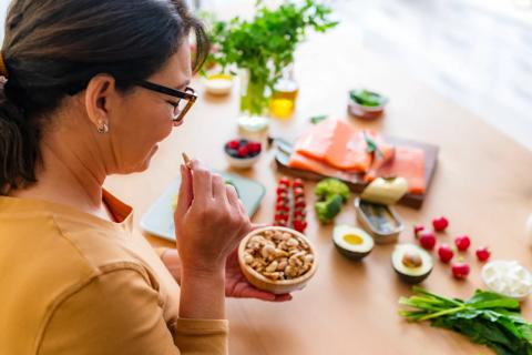 Person standing over table a food, holding small assorted bowl of nuts