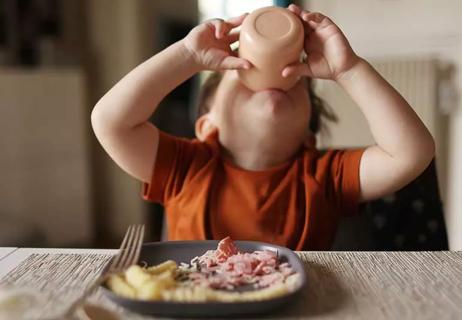 Toddler drinking from a cup while at the table during dinner.