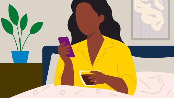 Person sitting up in bed, under the covers, scrolling on phone and holding a cup of coffee