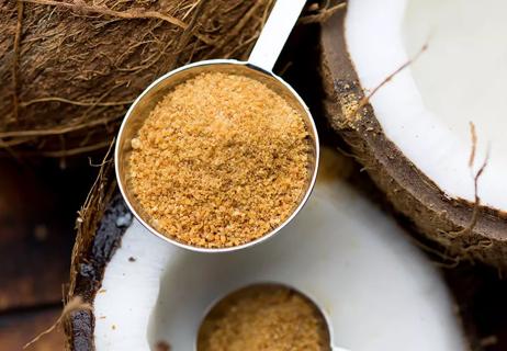 Closeup of caramel colored coconut sugar with halved coconuts in background.