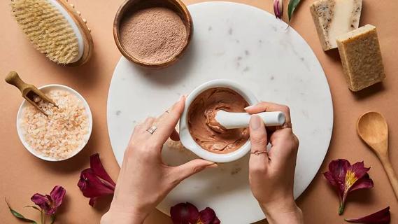 hands using mortal and pestle with cocoa powder, surrounded by soaps and bath salts