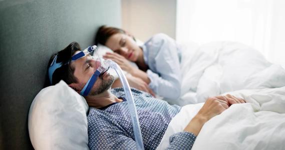 Couple asleep in bed, with one person wearing a CPAP machine mask