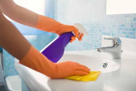 Gloved hands cleaning bathroom sink with spray bottle