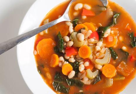 Closeup up of vegetable soup with tomatoes and kale in a white bowl.