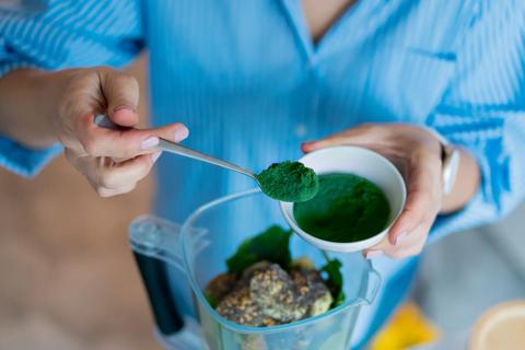 Person adding spirulina powder to a blender
