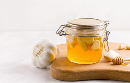 Jar of honey and fresh garlic on cutting board
