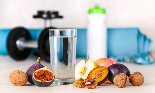 Glass of water and waterbottle, and figs, plums, walnuts and apples, with weights nearby