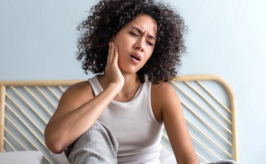Person sitting up in bed in the morning, holding side of face with jaw pain