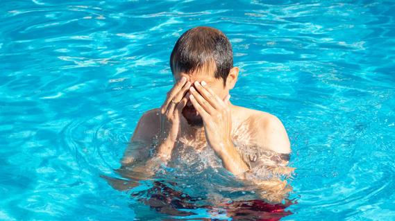 Person standing in pool, rubbing their eyes