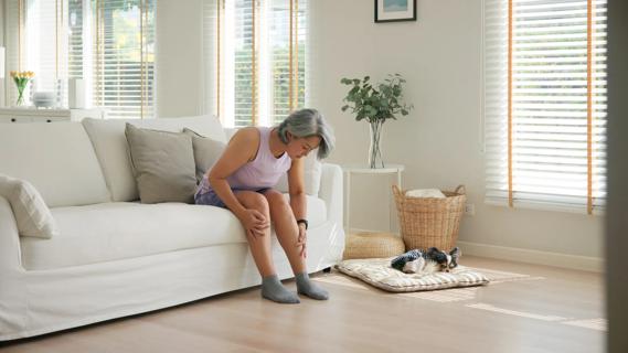 Person sitting on couch at home, bent down, rubbing their legs