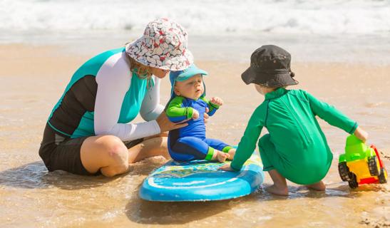 Woman and children wearing UV protective clothes at the beach.