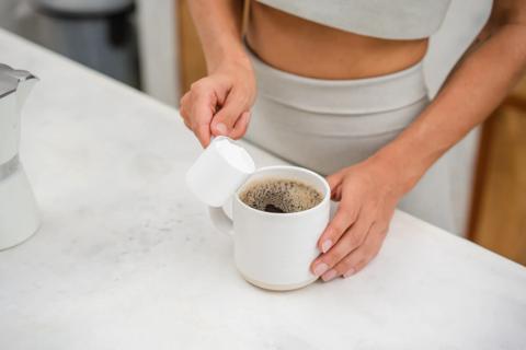 Person pouring a scoop of protein powder into a mug of coffee