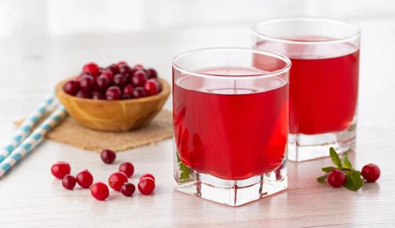 Two glasses of cranberry juice, with two paper straws and a bowl of fresh cranberries on the table