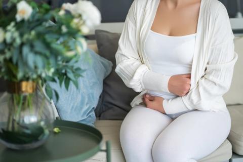 Woman sitting on couch with arms across her abdomen to hide it