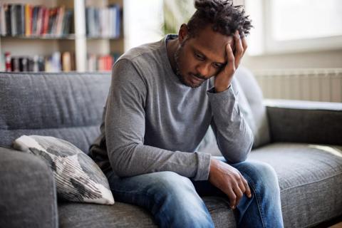 Male sitting on couch with head in hand, looking forlorn