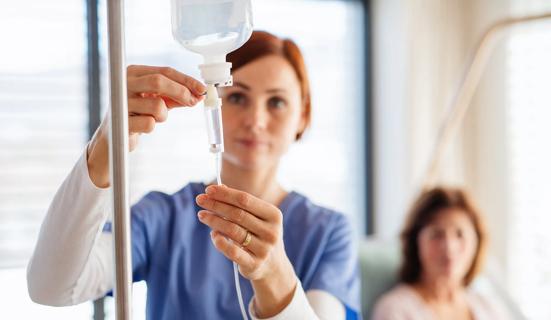 Healthcare provider adjusting IV fluid, with patient nearby