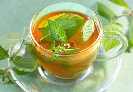 Spearmint tea in a glass see through cup with spearmint leaves scattered on the saucer and background.