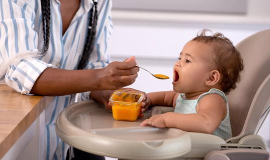 Caregiver feeding baby food to child in highchair