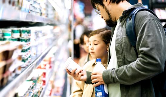 Child and caregiver read food labels in dairy case in grocery store