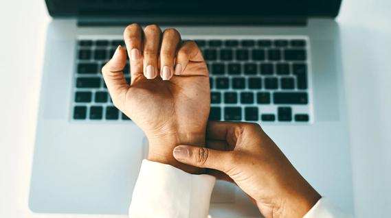 Hand applying pressure to wrist on other hand, hovering above keyboard