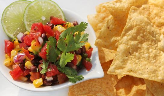 Black bean and corn sasla in dish, with lime garnish and tortilla chips