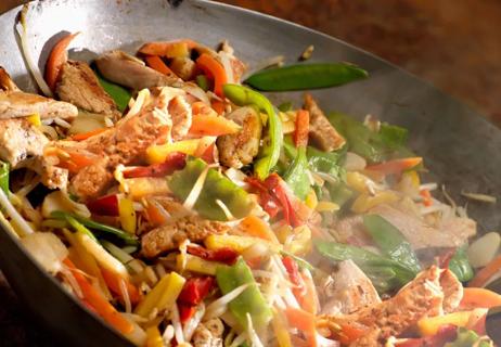 A sizzling wok of chicken stir fry with snow peas, cabbage and peppers