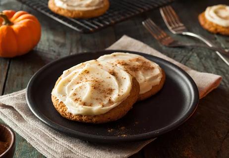 Black plate of two iced pumpkin cookies topped with cinnamon