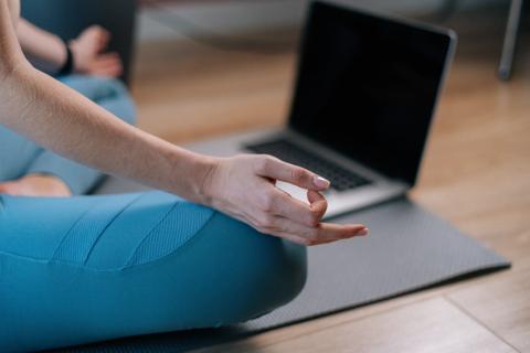 A woman practices yoga virtually using a computer.