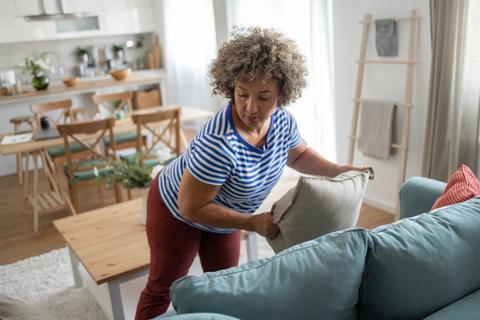 Person arranging pillow on couch in living room area