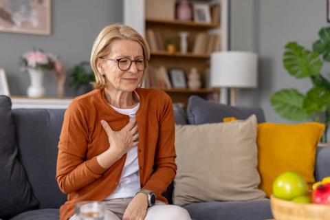 Older person sitting on couch, cringing, with hand on chest