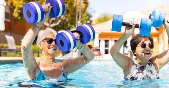 Two older people with foam weights doing water areobics in the pool