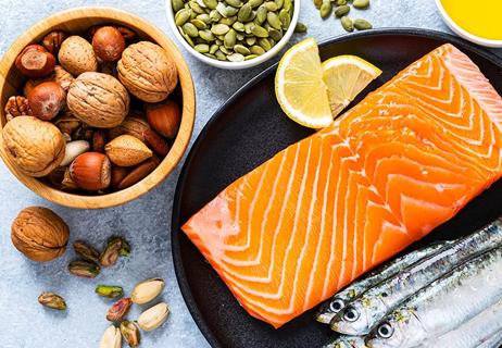 Samples of healthy protein; shown are nuts, seeds, and salmon, displayed on a bluish white marble table.