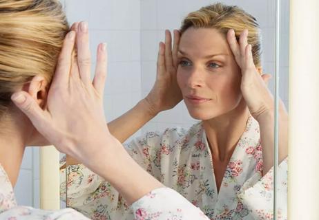 Woman looking in mirror and pulling skin until wrinkles disappear
