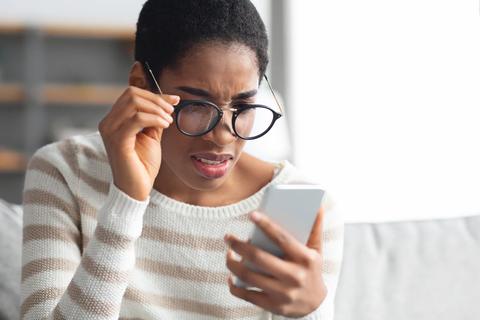 Person wearing glasses, struggling to read their cellphone