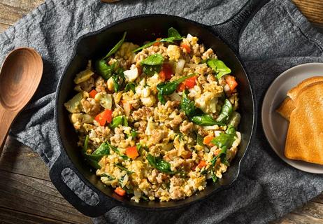 A cast-iron skillet filled with scrambled eggs, herbs and tomatoes