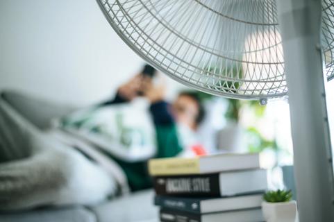 Person lying on couch, looking at smartphone, with fan blowing on them