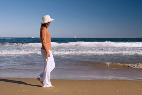 person walking along shore wearing sunhat and long-sleeve clothing
