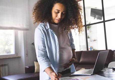 Pregnant person standing at desk working, hand on belly