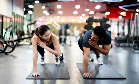 Two people look at each other while in a push-up position on exercise mats, crossing their left arms to their right shoulders