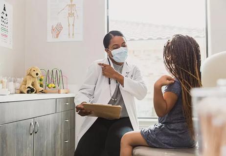 Masked doctor and child point at their shoulders during appointment