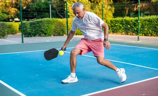 Older person playing pickle ball on outside court
