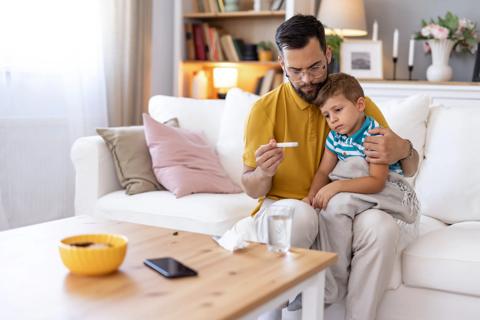 A parent checks a child’s thermometer while sitting on a couch