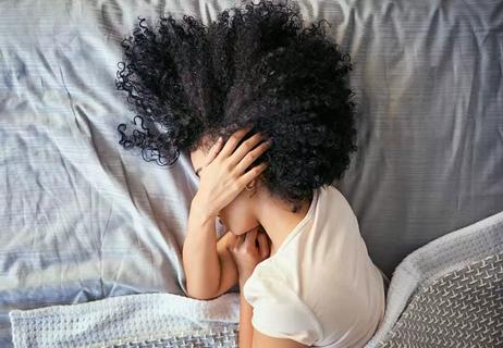 person in bed holding head with migraine