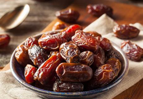 A white bowl placed on a wooden table filled with dried dates for snacking.