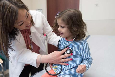 Physician smiles with child while using stethoscope